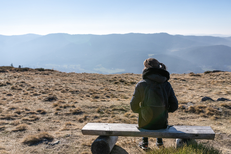 Young unrecognizable woman sitting an a bench on a mountain peak. Osser, upper bavarian forest, germany.の写真素材