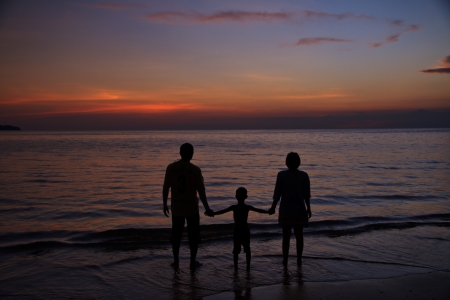 Silhouette of two adults and a child at the coastの写真素材