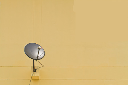 Black satellite dish on yellow wall background の写真素材