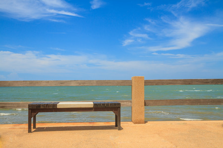 Wooden bench seat on stone floor near sea and blue sky.