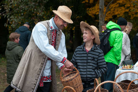Belarus, urban village Glusha - October 5, 2019. A man in a straw hat and a folk costume with a young boy and his products - wicker baskets of straw. Ethnic craft.のeditorial素材
