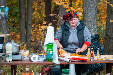 Belarus, urban village Glusha - October 5, 2019. A colorful woman prepares food, stuffed pancakes, at a traditional autumn, folk harvest festival. Cuisine of the world.のeditorial素材