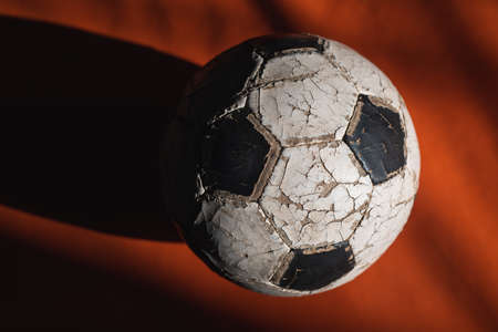 Old cracked soccer ball on a dark background in a beam of light.の写真素材