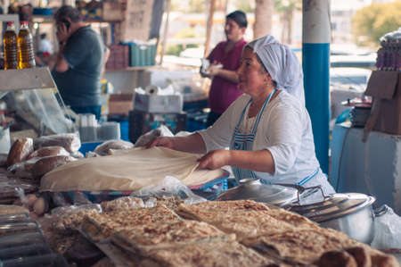 Bodrum, Turkey - August 23, 2019. Beautiful Turkish woman makes and sells cakes, pita bread, pastries in an open-air market.のeditorial素材