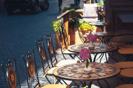 Tables of a casual cafe with pink cute flowers on the tables of the pedestrian street of the old city.の写真素材