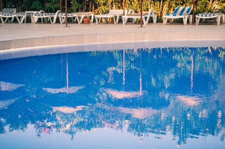 Transparent blue pool with sun loungers in the early morning at the resort at the hotel. Reflection in umbrellas and greenery in calm water.のeditorial素材