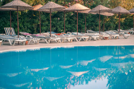Transparent blue pool with sun loungers in the early morning at the resort at the hotel. Reflection in umbrellas and greenery in calm water.のeditorial素材