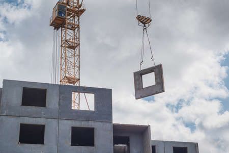 A construction crane on the background of the sky with clouds carries the building blocks. Housing construction.の写真素材