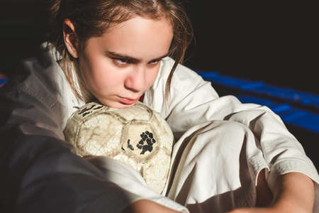 Martial arts training. Beautiful teen girl in a white kimono with a shabby soccer ball is resting after the game.の写真素材