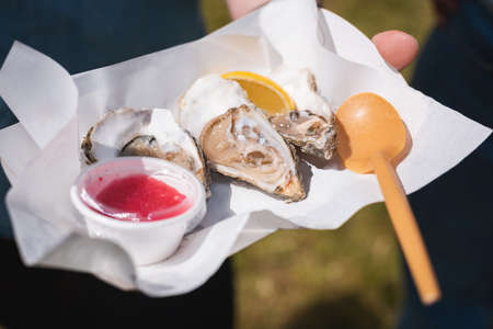 Delicious fresh oysters with lemon and sauce on a napkin. City picnic. Street food at mass events.の写真素材