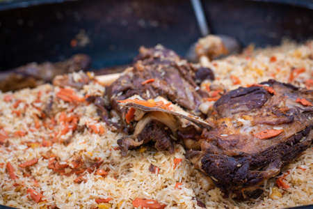A mountain of delicious rice pilaf with large pieces of meat in a cauldron on a fire in the open...