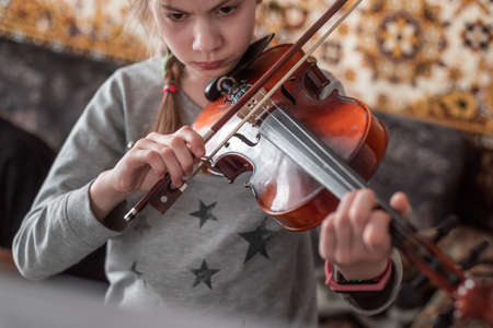 Beautiful teenager girl rehearses the violin at home. Music lessons in isolation during quarantine.の写真素材