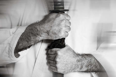 Male hands hold a Japanese katana sword against the background of a white kimano. Black and white...