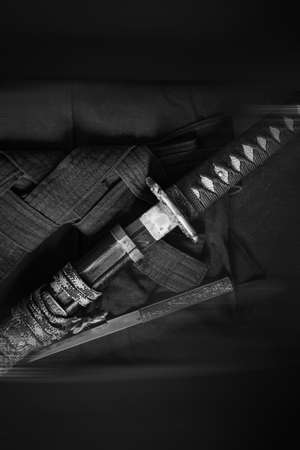 A katana sword with a braided handle on a traditionally folded hakama. Black and white vintage photo with blur.の写真素材