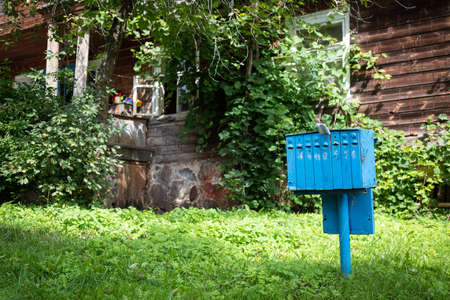 An old blue iron mailbox for mail and correspondence in a village near a house overgrown with greenery.の写真素材