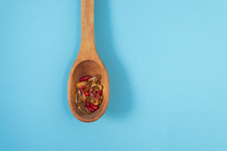 Wooden spoon with capsules and tablets on a blue background vertically with place to insert text. medicine and health.の写真素材