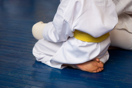 A young karate man with a yellow belt on a blue wooden floor in the hall of a sports school with his back to us.の写真素材