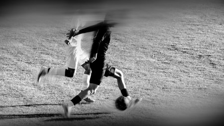 Black and white background with motion-blurred silhouettes of football athletes fighting for the ball.の写真素材