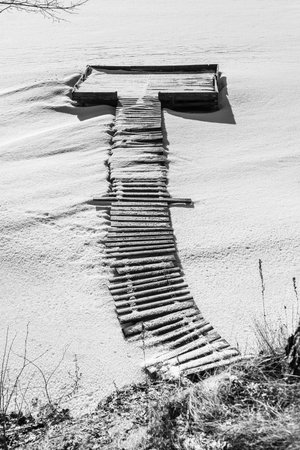 Fishing wooden bridges frozen and covered with snow on the icy surface of the lake.の写真素材