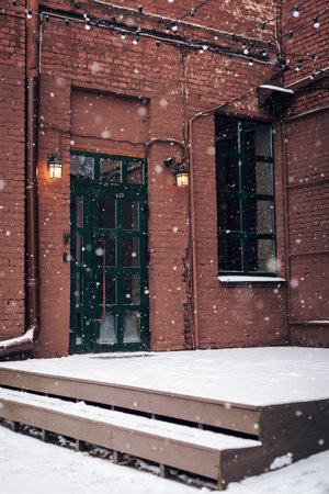 Wooden door, entrance to a brick building on the street in snowfall.
