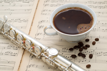 Silver flute, cup of coffee and coffee beans on an ancient music score background の写真素材