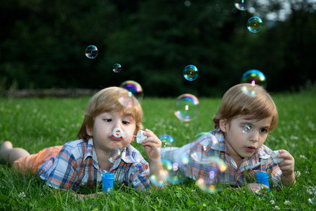 Little Twin Brothers  Blowing Soap Bubbles on Green Grass in Summer Park の写真素材