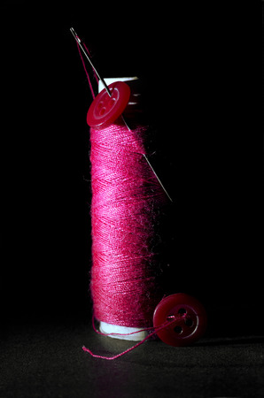 Spool of Red Thread with Needle and Red Buttons Isolated on Black Background