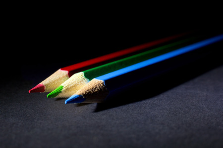 Macro Shot of Red, Green and Blue Sharpened Colorful Pencils Coming from Corner Against Black Background. Instruments for writing or drawing, consisting of a thin stick of graphite enclosed in a long thin piece of woodの写真素材
