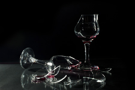 Red Wine in Broken Glass Cups Spilled on the Glass Table Isolated on Black Backgroundの写真素材