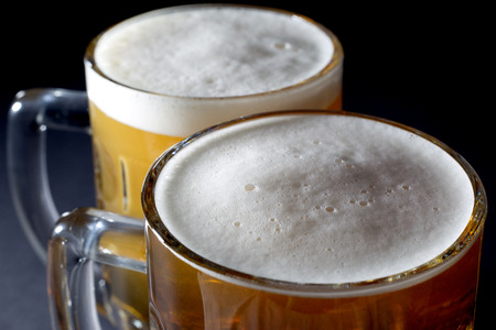 Closeup of Fresh Beer with Foam  in Two Beer Glasses Over Black Backgroundの写真素材