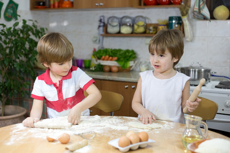 Two Little Boys Playing with Dough at the Kitchen Table at Homeの写真素材