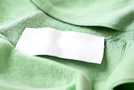 Blank white clothing label on green cotton shirt. Mockup for design