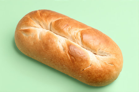 Freshly baked loaf of bread on a light green background, top view