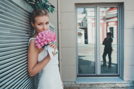 Portrait of beautiful bride with tulips. Wedding make up. The groom on the background of window.の写真素材