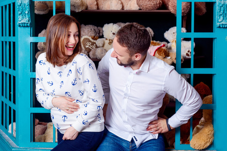 Young happy pregnant woman with husband. In the children's room on the background of toys. Wife...