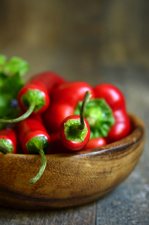 Chili pepper and bell pepper with greens in a wooden bowl.の写真素材