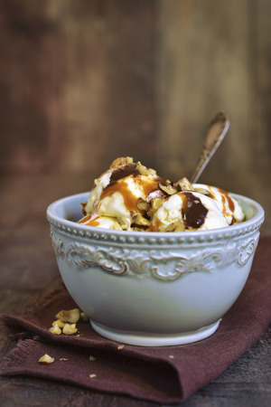Vanilla ice cream with nuts,chocolate and caramel in a blue vintage bowl on a rustic wooden background.の写真素材