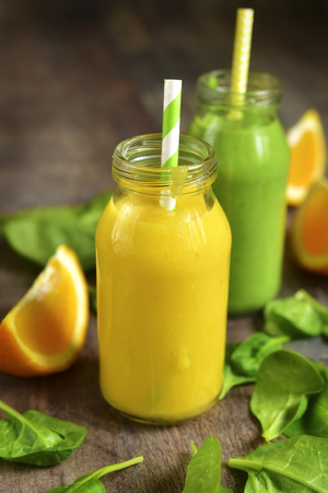 Two variations of fruit and vegetable smoothies in a bottle on a rustic wooden background.の写真素材