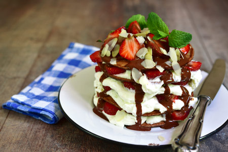 Chocolate pancakes with ricotta and strawberry on a white vintage plate on rustic wooden background.の写真素材