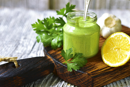 Spicy yogurt sauce with herbs in a glass jar on rustic wooden background.の写真素材