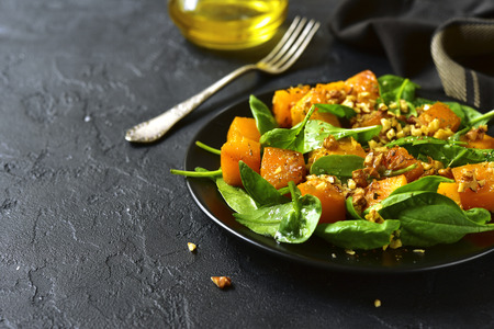 Roasted pumpkin salad with spinach and walnut on a black plate on a stone background.Space for text.の写真素材