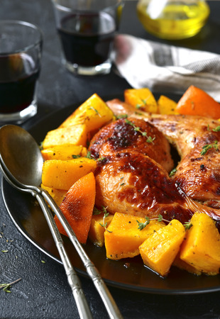 Chicken legs baked with pumpkin and orange on a black plate on a stone,concrete or slate background.の写真素材