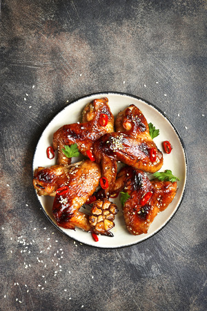 Spicy chicken wings with teriyaki sauce and sesame seeds on a vintage plate on a dark slate,stone or metal background.Top view with space for text.の写真素材