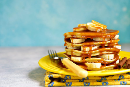 Banana pancakes with caramel for a breakfast on a yellow plate on a blue backcground.の写真素材