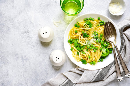 Spring spaghetty with broccoli and green pea on a white plate on a grey slate,concrete or stone background.Top view.の写真素材