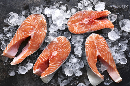 Steaks of raw salmon on ice on a dark slate,stone or metal background.Top view with space for text.の写真素材