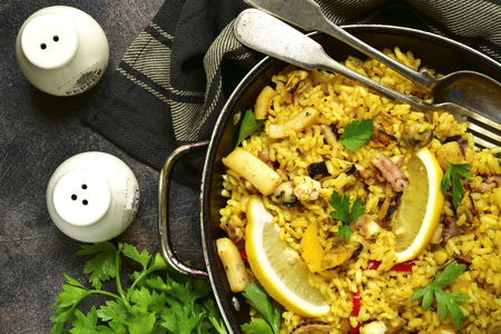 Traditional spanish (valencian) dish paella - stew with rice and seafood in a pan over dark rustic slate,stone or metal background.Top view.の写真素材