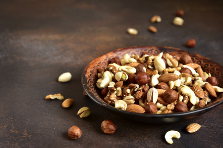 Assortment of nuts in a clay bowl on a dark rustic slate,stone or concrete background.の写真素材