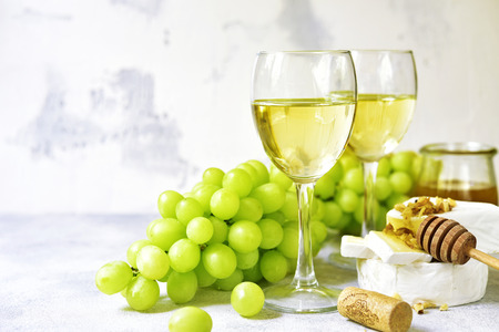 Two glasses of white wine,cheese and grapes on a light cocncrete,stone or slate background.の写真素材