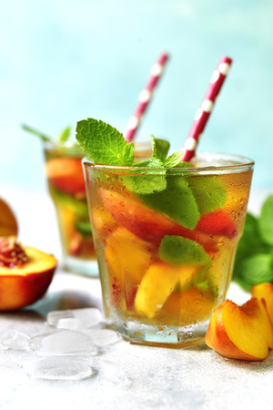 Peach iced tea with mint in a glass on a light background.の写真素材